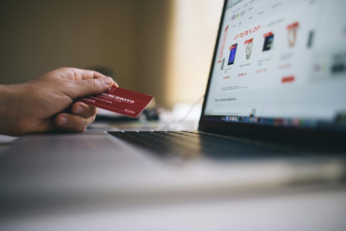 Personne tenant une carte de crédit tout en faisant des achats en ligne sur un ordinateur portable, ce qui indique des transactions de commerce électronique.